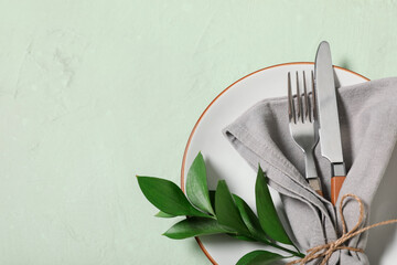Beautiful table setting with silver cutlery and fresh leaves on green background