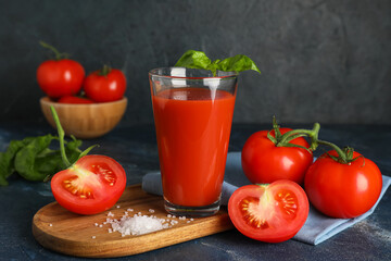 Glass of fresh tomato juice with basil and vegetables on dark background