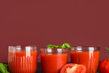 Glasses of fresh tomato juice with basil on color background