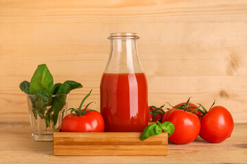Bottle of fresh tomato juice with basil and vegetables on wooden background