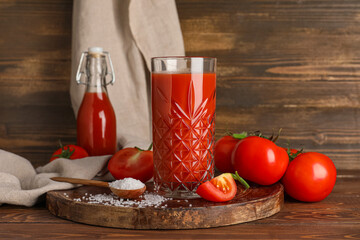 Glass of fresh tomato juice and spoon with salt on wooden background