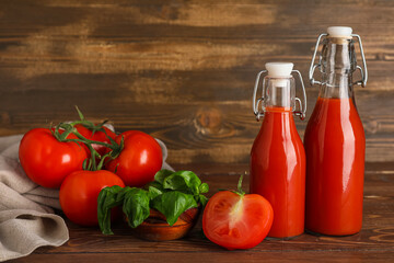 Bottles of fresh tomato juice with basil and vegetables on wooden background