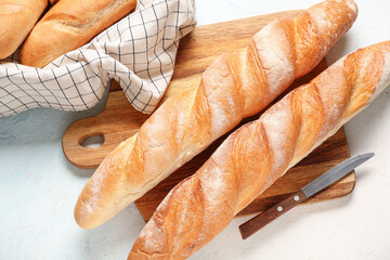Wooden board with fresh baguettes on light blue background