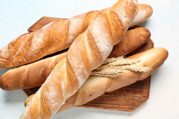 Wooden board with fresh baguettes and wheat on light blue background