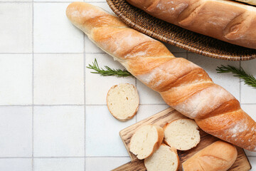 Wooden board and wicker bowl with fresh baguettes and rosemary on white tile background