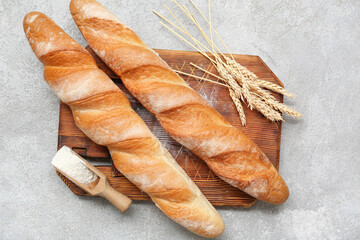 Wooden board with fresh baguettes, wheat and scoop of flour on grey background