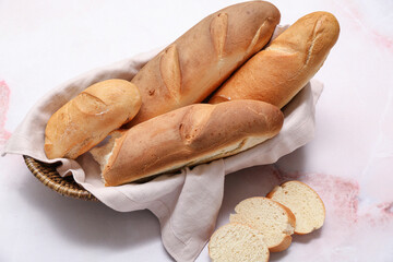 Wicker bowl with fresh baguettes on white marble background
