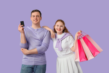 Beautiful young couple with shopping bags and credit card on lilac background