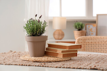 Pot with beautiful lavender flowers and books on table in stylish living room, closeup