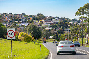 A hilly street in Geelong, Australia, with cars driving through, a 60 km/h speed limit sign and...