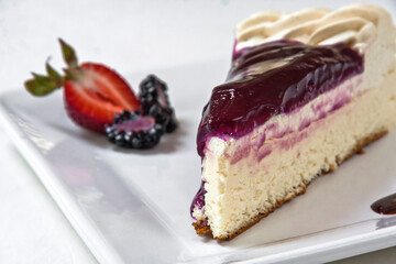 Cheesecake topped with blackberry sauce decorated with red berries and custard on a white background, slice of cake