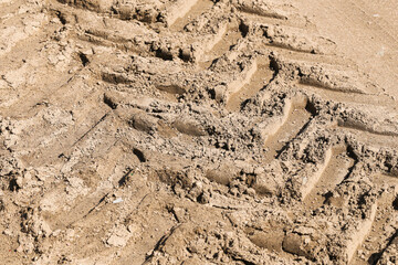 Heavy tire tracks in sand. Construction vehicle imprint. Deep tread pattern detail. Dry ground with...