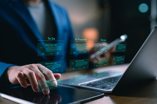 Businessman managing digital project workflow using futuristic virtual interface on tablet and laptop. Agile development, kanban board, task management, and remote work technology concept