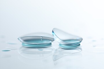 Pair of contact lenses and water drops on white mirror surface, closeup
