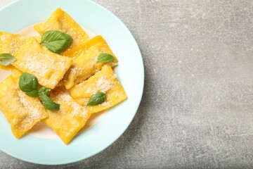 Delicious ravioli with cheese and basil on grey table, top view. Space for text