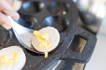 A vendor uses a spoon to serve cooked khanom krok on a hot plate with holes, khanom khrok, thai dessert