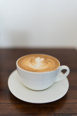 A cup of steaming coffee with latte art on a wood table at cafe