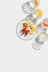 Crystal glasses with citrus slices in water on white background with reflections at sunlight, modern, minimal composition with clear glass cups with water, citrus fruit as lemon, orange on plate
