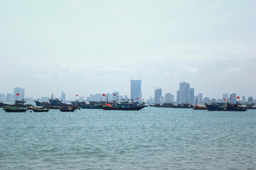 Naklejka premium Small fishing boat sailing on calm sea with a large city skyline in the foggy. Danang, Vietnam.