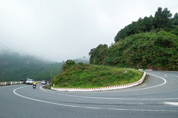 Lone Motorcycle Rider Navigating a Winding Road Through Mountains Under Foggy Sky. Prao, Vietnam.