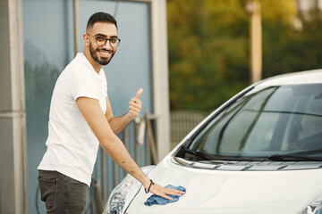 Indian man wiping his white transportation on car wash after washing