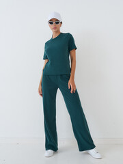 Fashion model poses elegantly in teal attire against a minimalist studio background