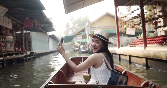 Young Asian tourist woman cheerful and happy to eat street food and sight seeing travel by boat along the canel at Damnoen Saduak Floating Market Thailand