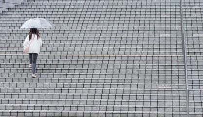 雨の日に傘を持って商業施設の階段を上る女性の姿