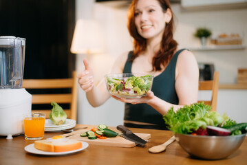 Smiling woman in a modern kitchen with fresh fruits, veggies, blender, and juice, embracing clean...