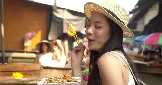Young Asian tourist woman cheerful and happy to eat street food and sight seeing travel by boat along the canel at Damnoen Saduak Floating Market Thailand