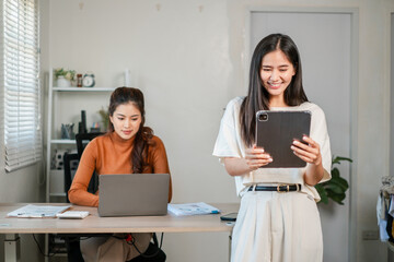 Two women in a modern office, using laptops and tablets, engaged in collaborative work and digital communication.