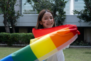 A joyful young woman waves a vibrant rainbow flag outdoors, celebrating diversity and inclusivity...