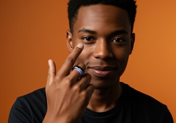 A stylish young man points at his eye while showcasing a smart ring with vibrant light.