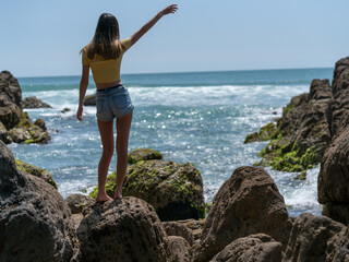 Girl in yellow top on coastal rocky seaside.