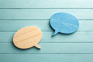 Two wooden speech bubbles, one natural wood and one blue, resting on a wooden background The image represents communication, dialogue, or discussion in a simple and modern way