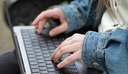 person is typing on a laptop with a blue jacket on. The person is wearing black pants