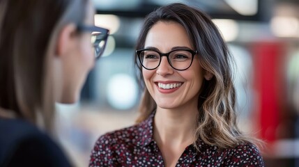 Smiling women in business casual attire with glasses engaged in a friendly conversation in a modern office