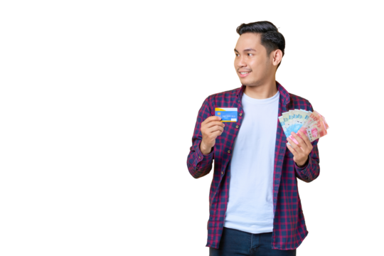 Smiling young Asian man in plaid shirt holding money banknotes and showing credit card, looking away at copy space isolated on transparent background