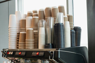 A large collection of disposable coffee cups stacked together in a cafe setting, featuring a mix of...