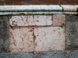 Textured weathered pink‑beige marble and brick wall plinth in historic Cremona building façade