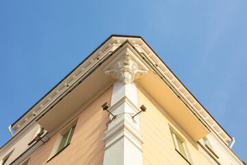 Architectural detail of a pastel-colored building corner with decorative features under a clear blue sky