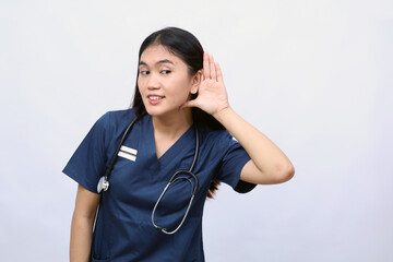 Young asian nurse woman isolated on white background listening to something by putting hand on the ear
