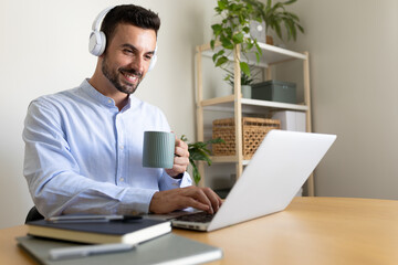 Fototapeta premium Caucasian man with headphones working at home office. Happy male entrepreneur using laptop.