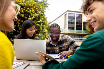 University students collaborating on project outdoors with laptop and tablet