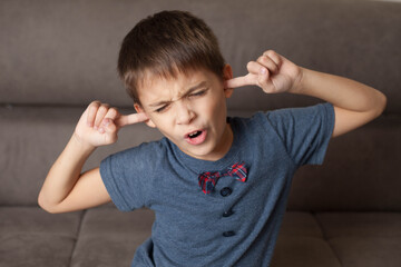 Close-up portrait of a Boy pulling a funny face with his eyes closed and his fingers in his ears