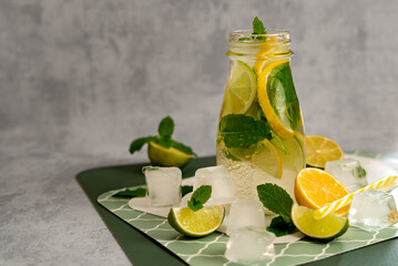 Citrus detox tea in a glass jar with lime, lemon, mint and ice cubes on a gray background. Concept of making summer lemonade.