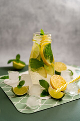 Cold detox tea with lime, lemon, mint with ice cubes and citrus fruits in front of a glass on a gray background. Concept of making summer lemonade. Cold drinks.