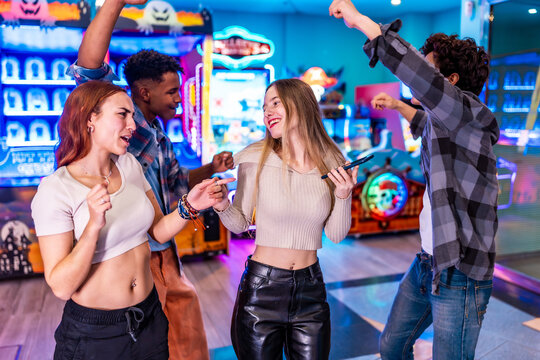 Multiethnic friends enjoying weekend playing arcade games and dancing