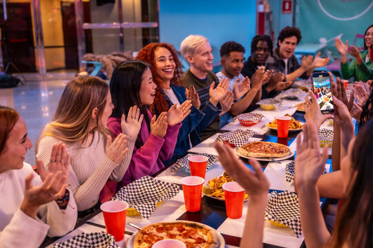 Happy multiethnic friends clapping and enjoying meal in bowling alley