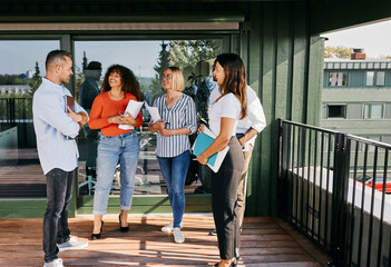 Team of smiling diverse professionals having a casual outdoor meeting on a sunny office terrace. Relaxed mood, modern work culture